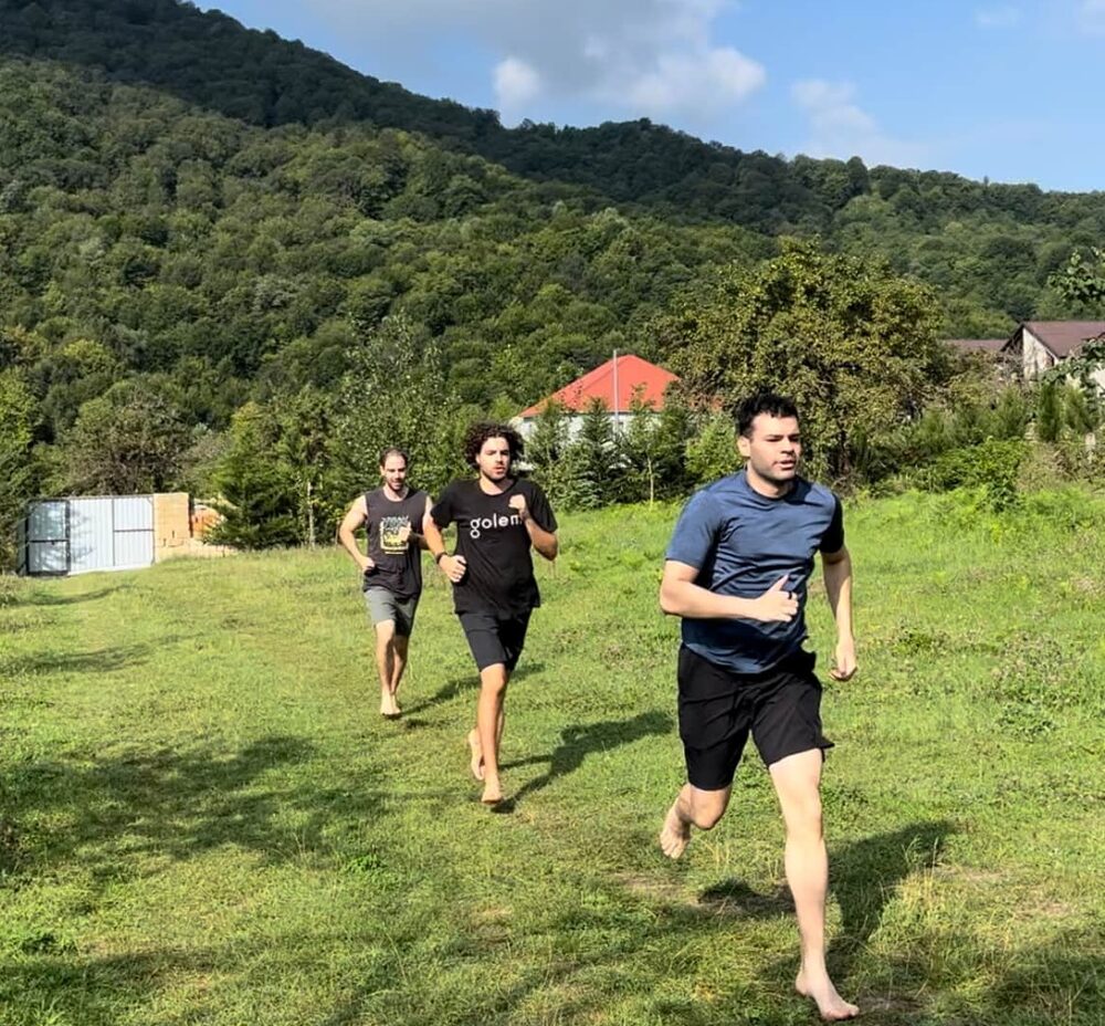 Three men running barefoot across a mountain meadow at Camp Hermes